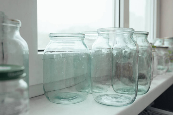 Muchos frascos de vidrio vacíos sin tapas de diferentes tamaños cerca de la ventana. Estilo de vida fotos. - Foto, Imagen