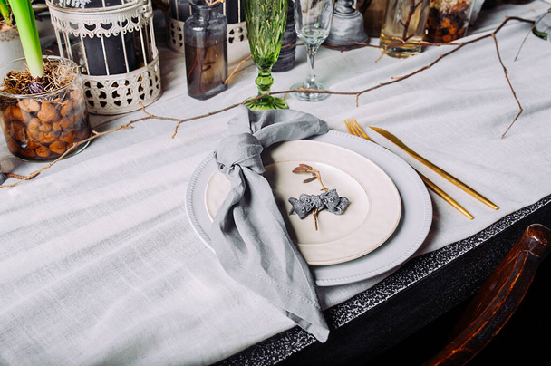 Накрытие стола в загадочном весеннем стиле с живыми растениями и ветвями. Белые тарелки с золотыми столовыми приборами и голубой салфеткой, завязанной в узел. - Фото, изображение