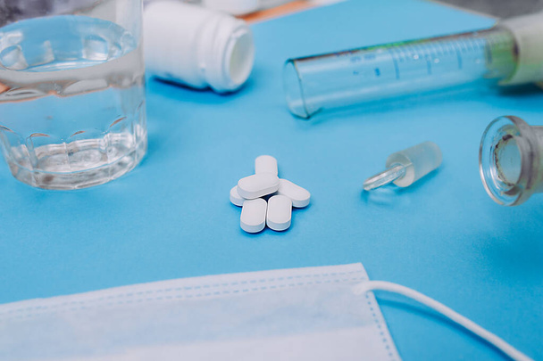 handvol grote witte capsules met tabletten op de achtergrond van medische hulpmiddelen, glazen glazen met water, bekerglas en medisch masker. Klaar lay-out coronavirus covid-19. - Foto, afbeelding