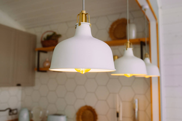witte kroonluchters aan het plafond met fel geel licht in een heldere Scandinavische keuken. - Foto, afbeelding