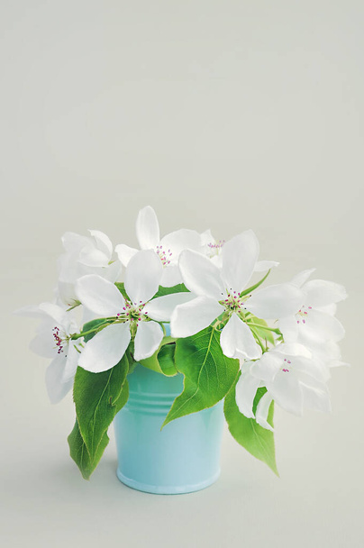 boeket van witte verse weelderige lente peer bloemen met grote groene bladeren in een blauwe metalen emmer. eenvoudige inrichting voor een gezellige plek. luchtzuivering door installaties - Foto, afbeelding