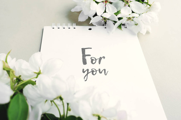 weißer Blanko-Notizblock auf einer Spirale mit einer Inschrift für Sie mit Sträußen weißer, üppig blühender frischer Birnenblüten auf hellgrauem Papierhintergrund. Urlaubs-Grußkarte - Foto, Bild
