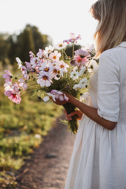 Back view of young woman with bouquet of flowers cosmos in hands. The concept of summer mood. High quality photo - Foto, imagen