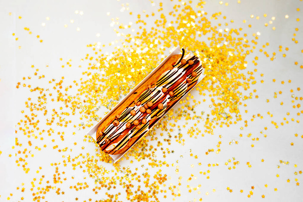 Caramel delicious fresh Eclair on a soft beige background with gold stars and sequins, top view, festive layout - Photo, Image