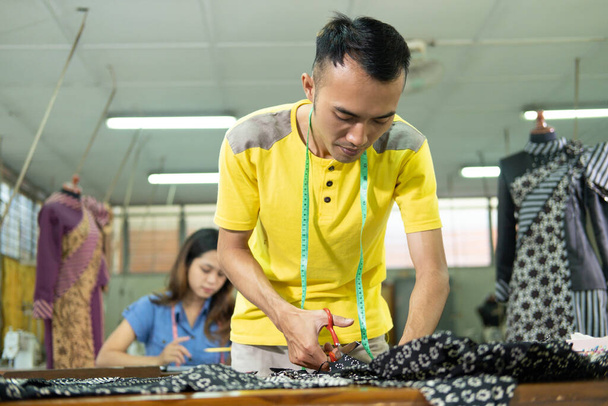 Asian man tailor standing when cutting a cloth pattern using scissor - Foto, Bild