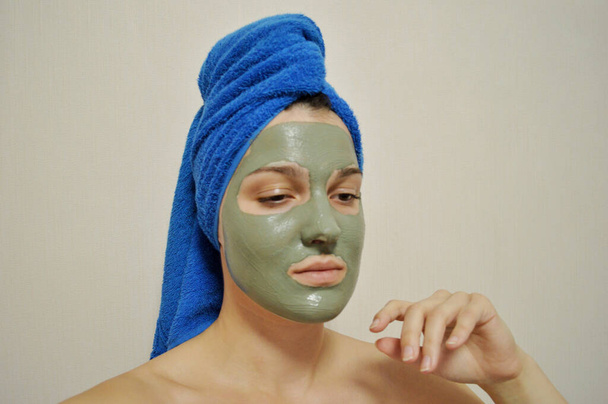 Γυναίκα με μπλε πετσέτα στο κεφάλι και πηλό μάσκα στο πρόσωπό της - Φωτογραφία, εικόνα