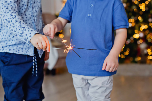 Wybiórcze skupienie. Dzieci trzymają Sparklera, zbliżenie. Sparkler i iskry Makro zdjęcie świąteczne bokeh tło, magiczna atmosfera na Boże Narodzenie i Nowy rok - Zdjęcie, obraz