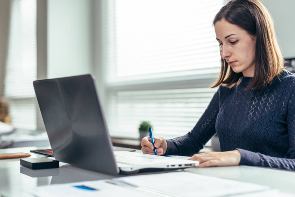 Woman working at her desk, taking notes. - Fotografie, Obrázek