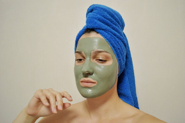 Женщина с синим полотенцем на голове и глиняной маской на лице - Фото, изображение