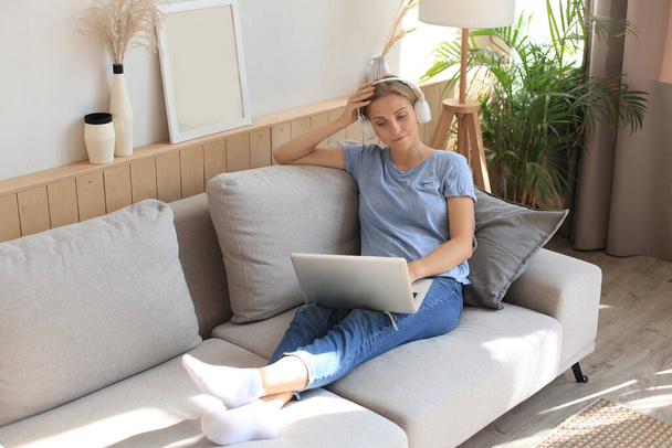 Smiling young woman with headphones and laptop on the sofa - Foto, Imagem