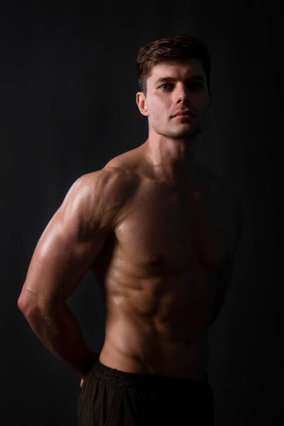 Muscular bodybuilder posing with a naked torso on a black background in the dark with backlight. Sexy man. - Photo, image