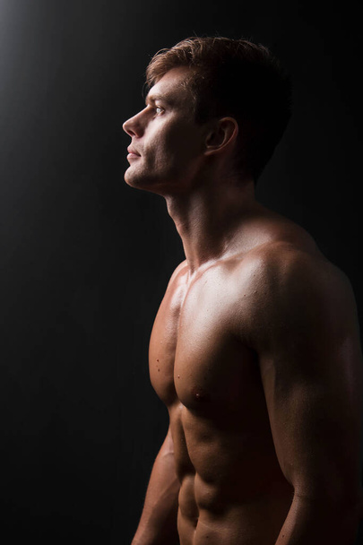 Muscular bodybuilder posing with a naked torso on a black background in the dark with backlight. Sexy man. - Foto, Imagem
