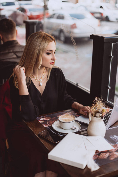 Beautiful young business woman with laptop enjoys a cup of coffee in a cafe during lunch break in autumn. Soft selective focus, artistic noise. - Foto, imagen