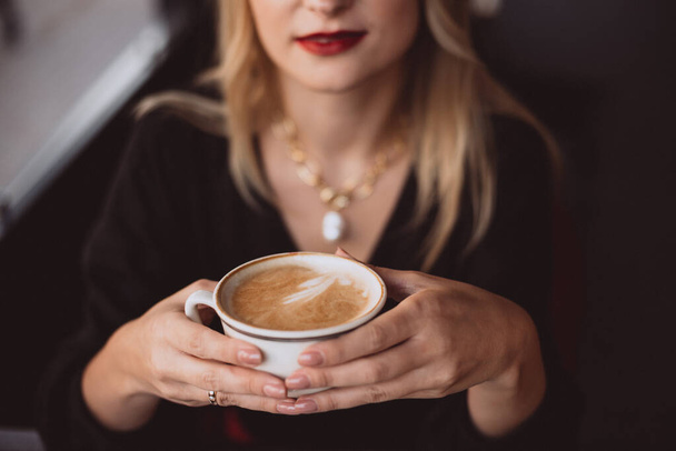 Die schöne junge Geschäftsfrau genießt in der Mittagspause im Herbst eine Tasse Kaffee in einem Café. Weiche selektive Fokussierung, künstlerisches Rauschen. - Foto, Bild