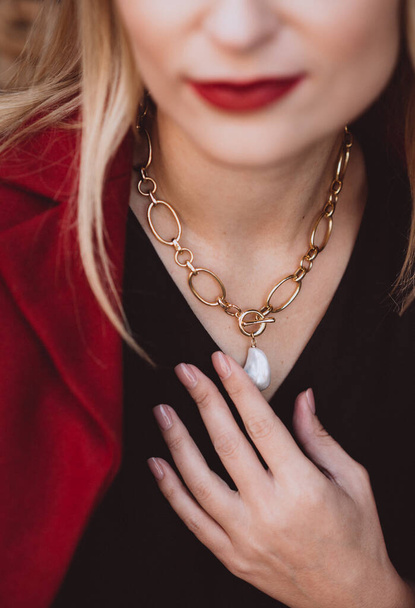 Beautiful young blonde woman in a trendy autumn dress in burgundy Marsala color with a necklace on her neck. Soft selective focus. Artistic noise. - 写真・画像
