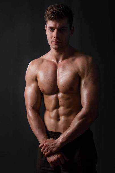 Muscular bodybuilder posing with a naked torso against a black background. Sexy man. - Photo, image