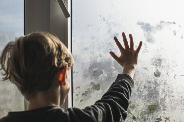 A little boy draws on a fogged, wet window in autumn - Photo, image