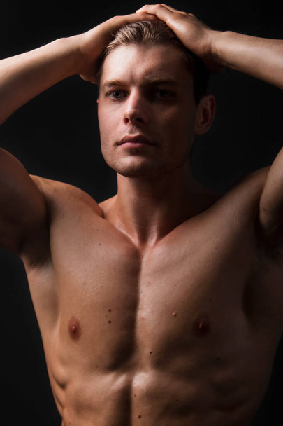 Bodybuilder holds muscular arms on head. Photo in studio on a black background. - Zdjęcie, obraz