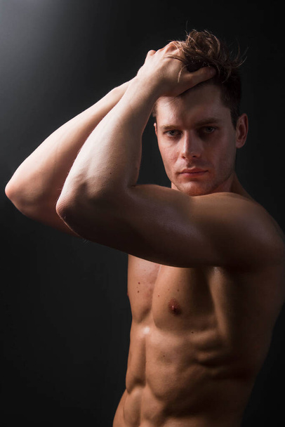 Bodybuilder holds muscular arms on head. Photo in studio on a black background. - Photo, image