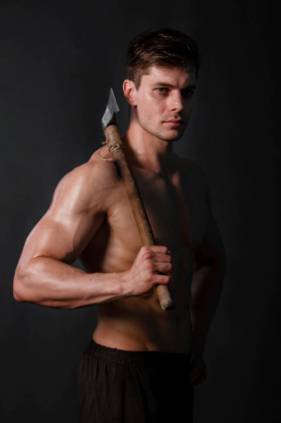 Bodybuilder with an ax in his hands on a black background. - Fotografie, Obrázek