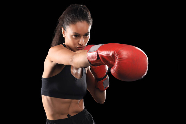 Kickboxing woman in activewear and red kickboxing gloves on black background performing a martial arts kick. Sport exercise, fitness workout - Foto, Imagem