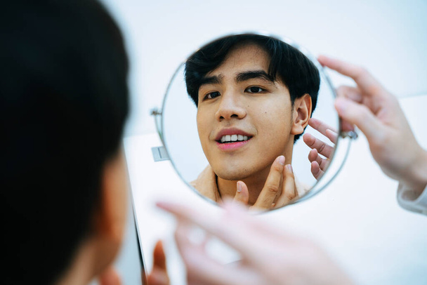 Asiático joven mirando a sí mismo en espejo tomando consejos de esteticista sobre el tratamiento facial. - Foto, Imagen