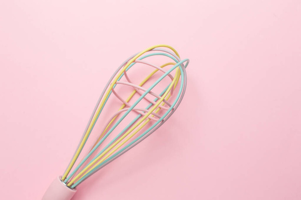 Multi-colored pastel kitchen whisk on pink background, cute kitchen utensils, feminine cooking top view - Foto, imagen