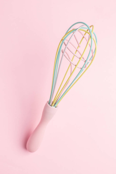 Multi-colored pastel kitchen whisk on pink background, cute kitchen utensils, feminine cooking top view - Photo, Image