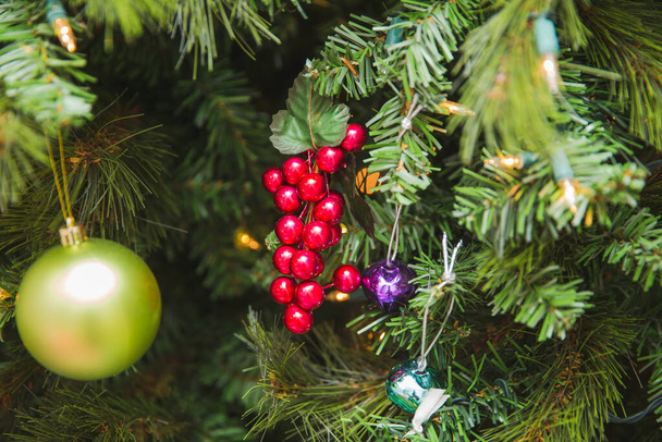 Dekorative rote Stechpalmenbeeren in der Nähe anderer Ornamente auf einem Weihnachtsbaum. - Foto, Bild