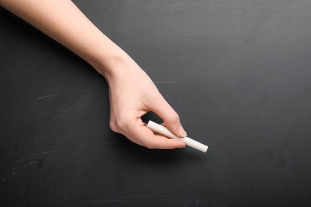 Female hand with piece of chalk on blackboard - Photo, Image