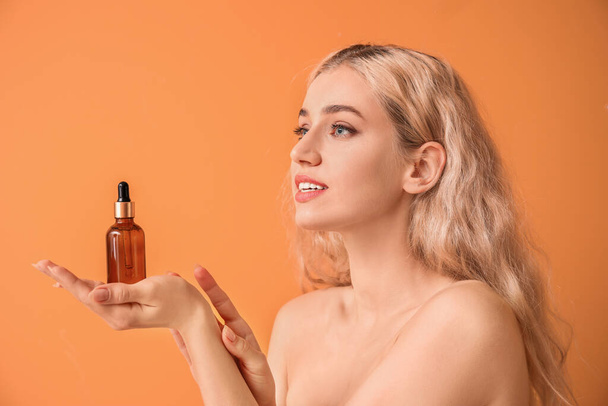 Mooie jonge vrouw met cosmetische olie op kleur achtergrond - Foto, afbeelding