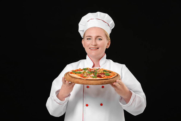 Esmer arka planda lezzetli pizzası olan olgun bir kadın şef. - Fotoğraf, Görsel