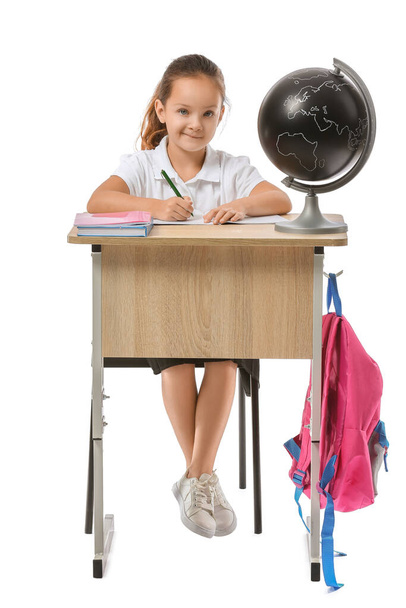Μικρή μαθήτρια κάθεται στο γραφείο του σχολείου σε λευκό φόντο - Φωτογραφία, εικόνα