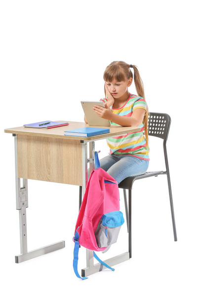Piccolo alunno con tablet seduto alla scrivania della scuola su sfondo bianco - Foto, immagini