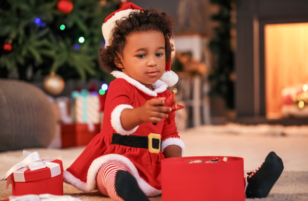 Cute African-American baby girl with gift at home on Christmas eve - Photo, Image