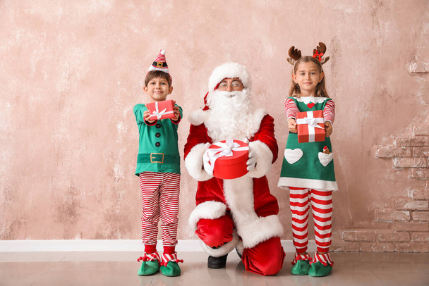 Roztomilí malí elfové se Santa Clausem a vánoční dárky v blízkosti barevné stěny - Fotografie, Obrázek