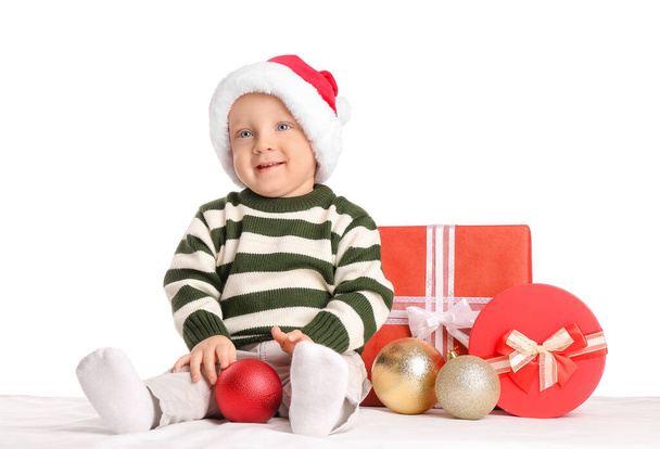 Симпатичный маленький ребенок в шляпе Санта-Клауса и с подарочными коробками на белом фоне - Фото, изображение