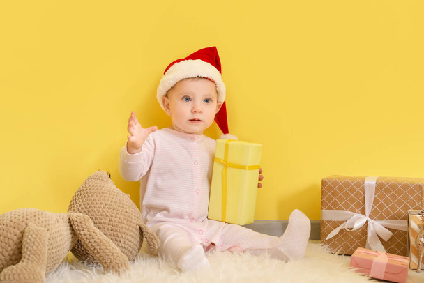Милый маленький ребенок с рождественскими подарками рядом с цветной стеной - Фото, изображение