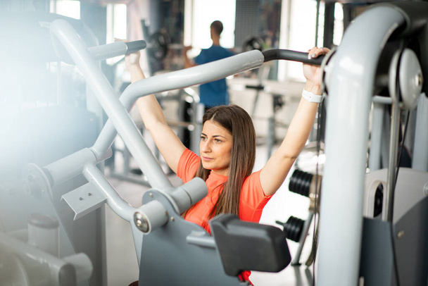 Pretty young woman using gym equipment for arm exercises - Photo, image