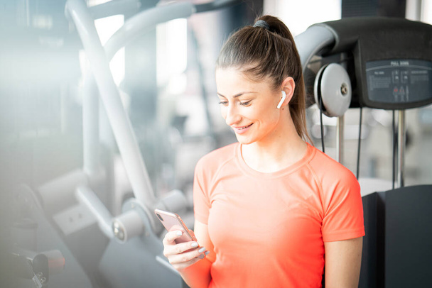 Young fit woman checking phone during workout break in gym - 写真・画像