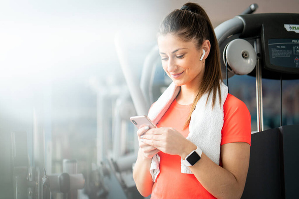 Young fit woman checking phone during workout break in gym - Foto, afbeelding