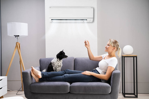 Happy Woman Sitting On Sofa Using Air Conditioner At Home - Фото, изображение