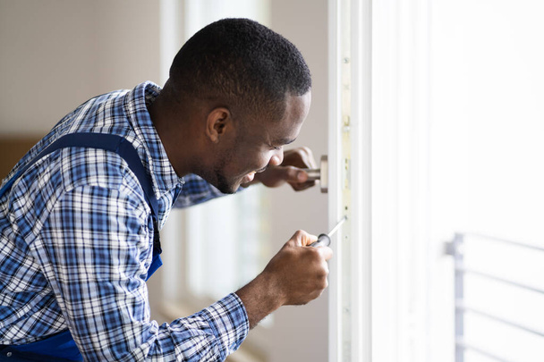 Young African Repairman In Overalls Installing Window - 写真・画像