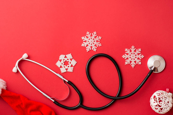 stethoscope and christmas decoration on red background, winter medicine card - Fotó, kép