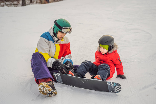 Snowboard instructor teaches a boy to snowboarding. Activities for children in winter. Childrens winter sport. Lifestyle - 写真・画像