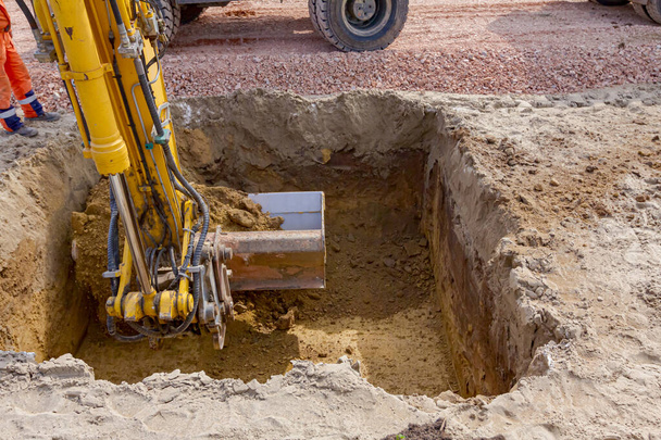 Visão baixa sobre as pernas dos trabalhadores como eles estão esperando para escavadeira para terminar de cavar trincheira quadrada no local de construção. - Foto, Imagem