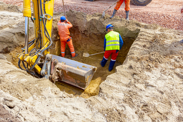 Workers are using shovels for realign excess of ground to correct trench measure. - Photo, Image