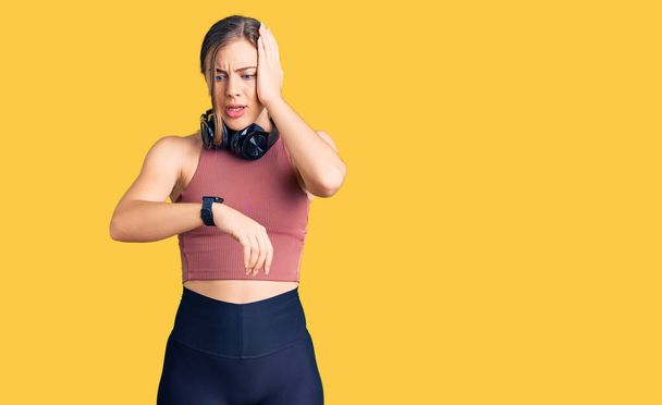 Beautiful caucasian young woman wearing gym clothes and using headphones looking at the watch time worried, afraid of getting late  - Photo, Image