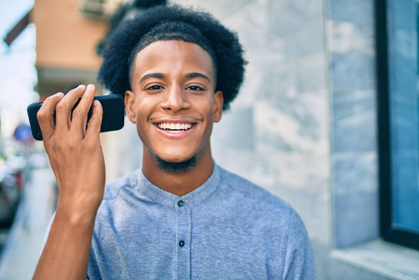 Młody Afroamerykanin słuchający wiadomości dźwiękowych za pomocą smartfona w mieście. - Zdjęcie, obraz