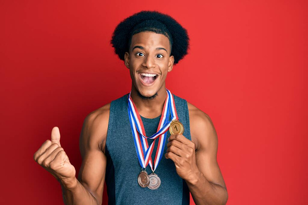 Uomo afro-americano con i capelli afro indossa medaglie vincenti urlando orgoglioso, celebrando la vittoria e il successo molto eccitato con il braccio sollevato  - Foto, immagini